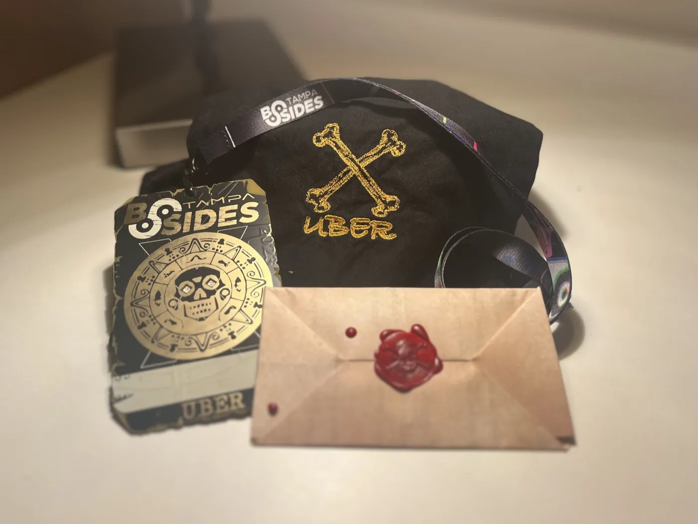 BSides Tampa Uber badge with gold Aztec skull design, embroidered crossbones bag, and wax-sealed envelope