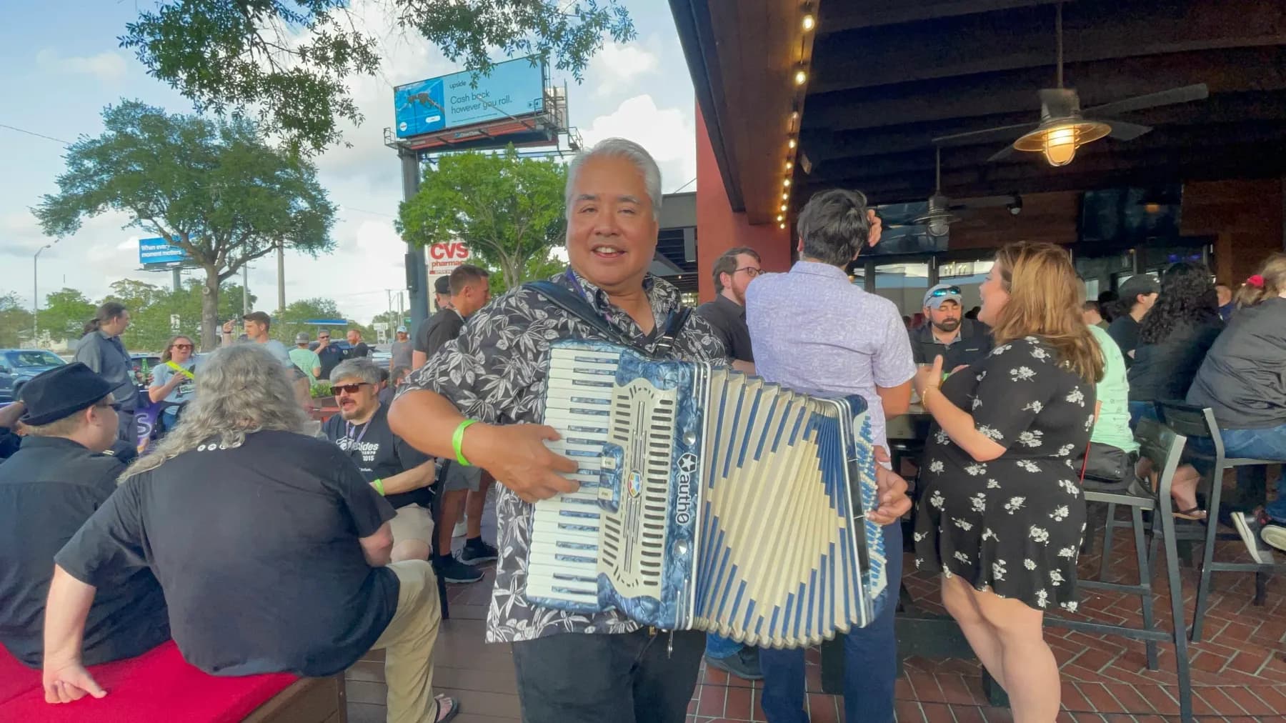 A BSides Tampa participant playing accordion on the patio while the crowd enjoys Happy Hour