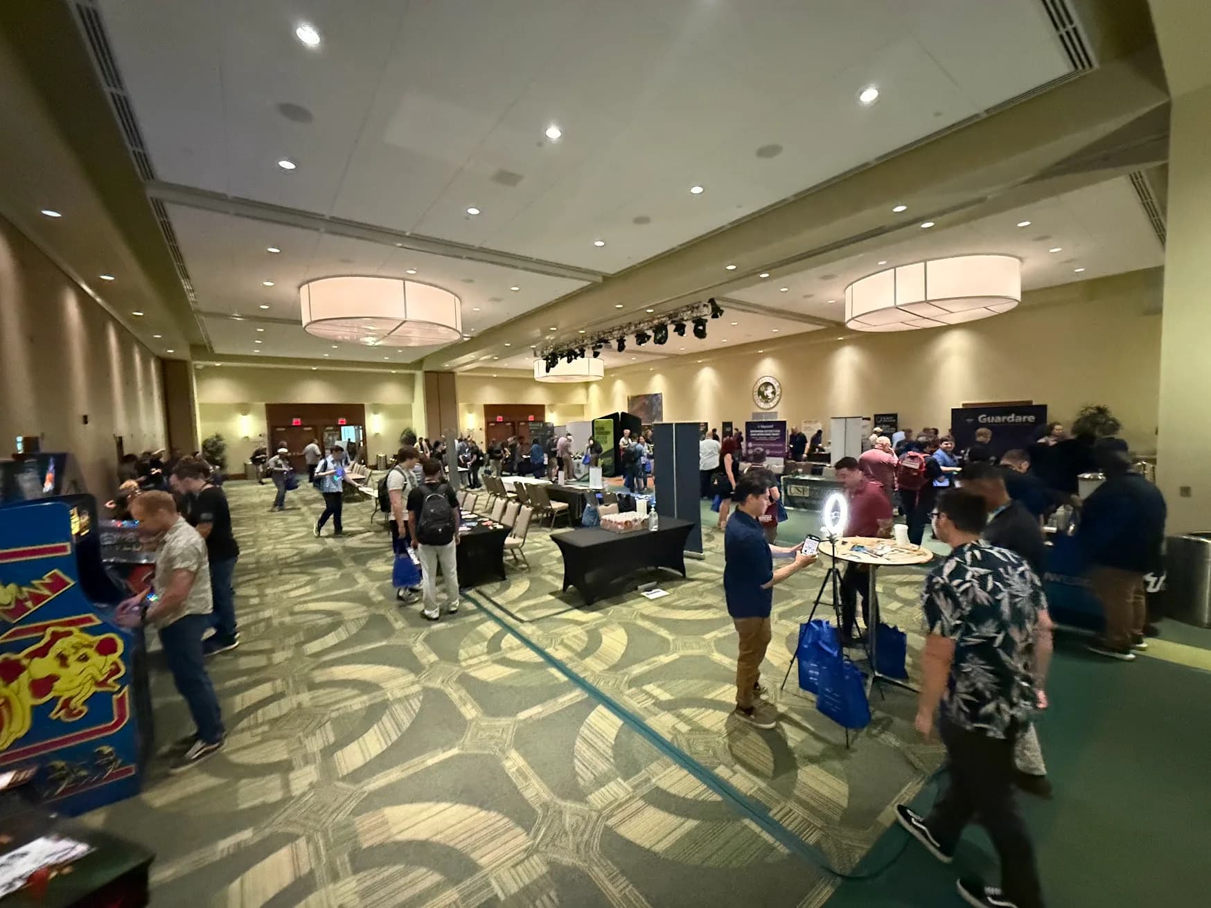 Expo hall with sponsor booths, energy & coffee stations, and attendees browsing